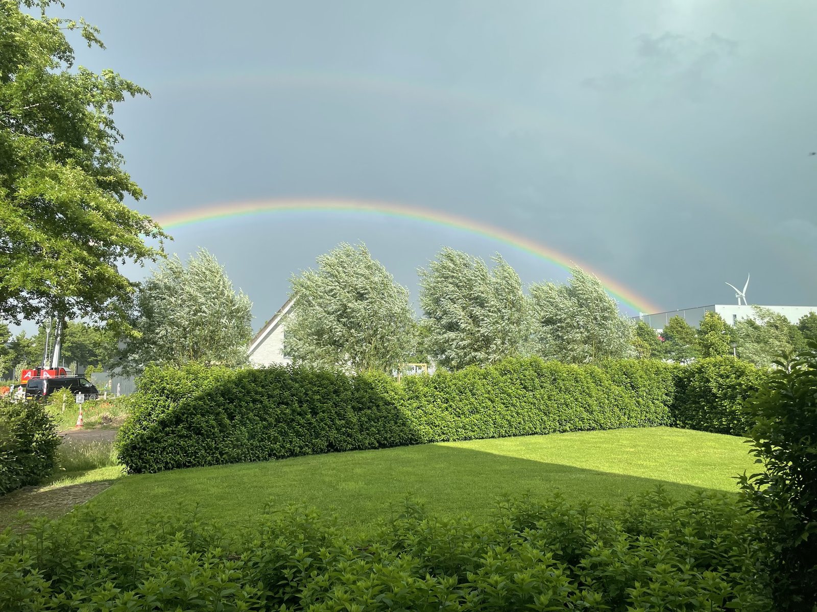 Groot gazon met een strak geknipte haag, met een dubbele regenboog boven de bomen