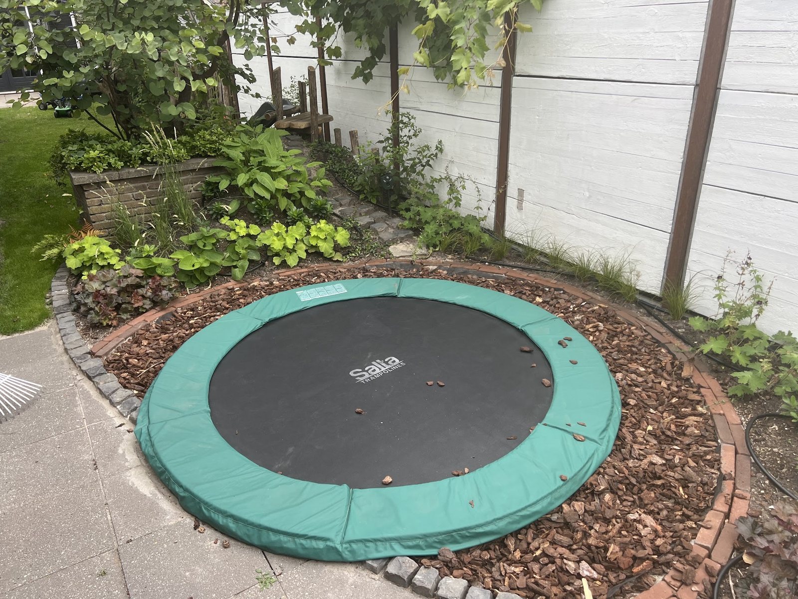 Ingegraven trampoline met een gebogen rand van klinkers en boomschors